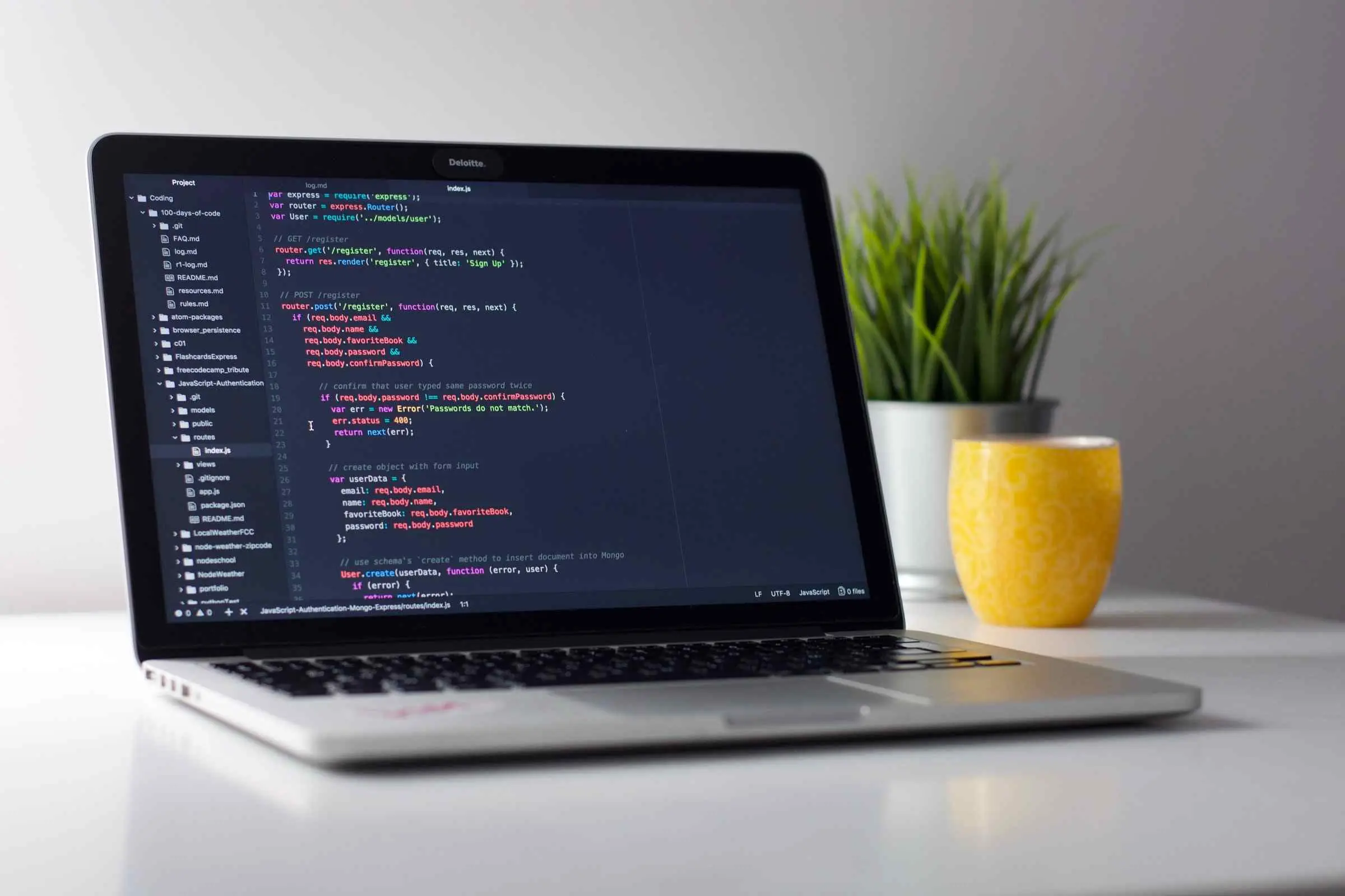 Un ordinateur montrant du code sur un bureau blanc avec une plante verte à l'arrière plan